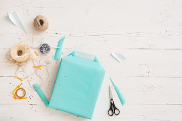 Top view on gift wrapping. Gift in paper of turquoise color. Gift ribbons, twine, scissors and gift...