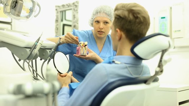 Dentist in uniform with maket of jaw is telling about healthcare in dental clinic