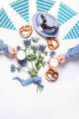 Modern Oktoberfest concept. Hand  in traditional blue shirt holding cups of draft beer, on white...