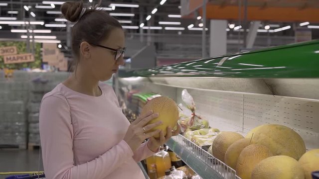 Young pregnant woman with glasses in a supermarket chooses fresh organic fruits. Woman choosing fruits while shopping at the supermarket.