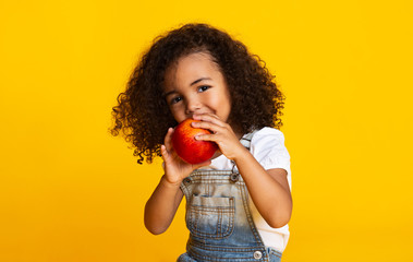 Yummy. Little afro girl eating red apple