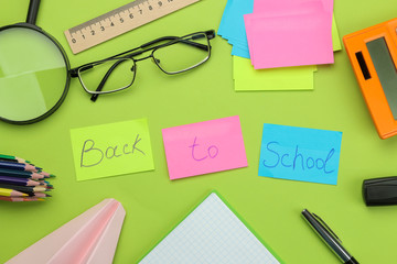 back to school. stationery, school supplies text on bright multi-colored stickers, a calculator, magnifier, and glasses on a bright green background. top view