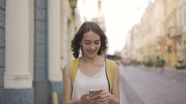 Happy excited young woman receiving discount for shopping while checking email box on mobile calling for sharing success with friend while walking in urban setting down street