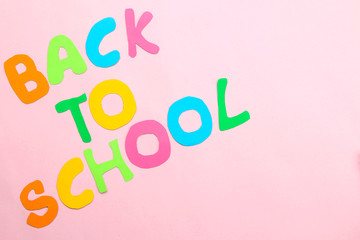 text back to school from multi-colored paper letters on a bright pink background. top view.