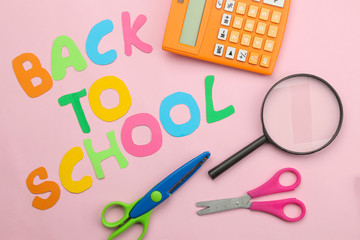 back to school. stationery, school supplies, text, scissors and a calculator with pencils on a bright pink background. top view.