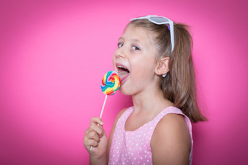 Happy smiling child with sweet lollipop having fun over colorful pink background
