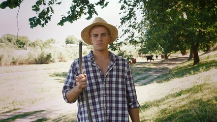 Portrait of young villager man shepherd in straw hat with his flock of cows on a rural background