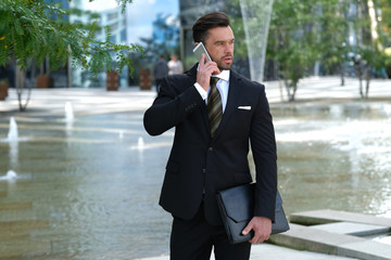 Businessman talking on the phone in front of his working place.