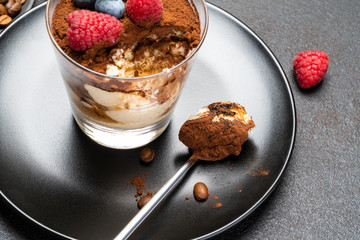 Classic tiramisu dessert portion with blueberries and raspberries in a glass cup on stone serving board on concrete background