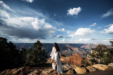 A girl in cowboy boots and a long white dress with stunning canyon landscape