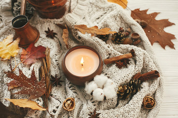 Fototapeta na wymiar Hygge lifestyle. Candle with berries, fall leaves, anise,herbs, acorns, nuts , cinnamon, cotton on white knitted sweater. Autumn mood. Hello autumn, cozy inspirational image