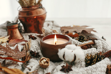 Hello autumn, cozy inspirational image.Hygge lifestyle. Candle with berries, fall leaves, anise,herbs, acorns, nuts , cinnamon, cotton on white knitted sweater. Autumn mood.