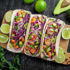Delicious tacos with shrimps, avocado, onion and lime on a wooden board. Classic Tex-Mex cuisine...