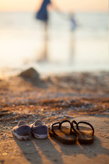 Children and adults beach sandals in the sand against the background of silhouettes of mother and...