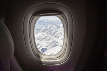 View of snowy mountains from a window of an airplane from inside