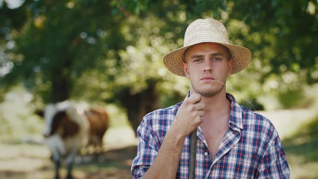 Portrait of young villager man shepherd in straw hat with his flock of cows on a rural background