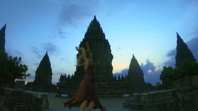 Woman in long dress is spinning at old ruins of Prambanan temple in Java island