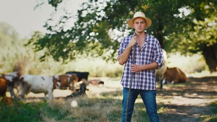 Young villager man shepherd in straw hat with his flock of cows on a rural background, slow motion