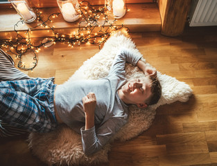 Boy lying on floor on sheepskin and looking in window in cozy home atmosphere. Peaceful moments of...