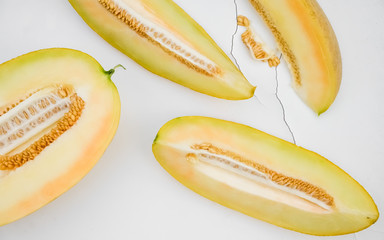 Yellow ripe sweet melon with seeds cut into pieces on white cracked in the background. 