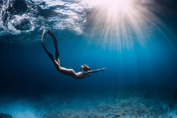 Woman freediver glides with fins. over sandy sea. Freediving and beautiful light in blue sea