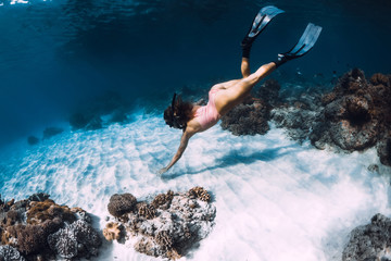 Woman freediver dive with fins near corals. Freediving underwater in blue ocean