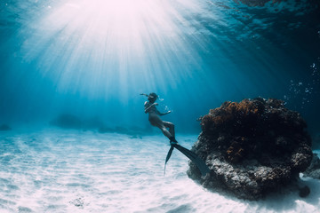 Free diver young woman with fins swim over sandy bottom underwater ocean