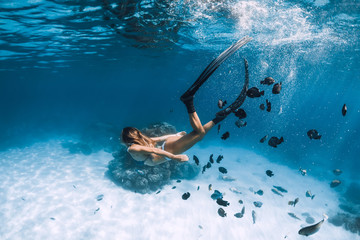 Woman freediver glides with fins over sandy sea with fishes in Hawaii