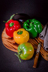 Pimientos verdes, rojos y amarillos sobre tabla de cortar junto a tomate verde y berenjena