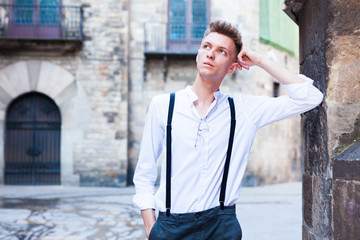 young European guy in shirt and trousers with suspenders walking around city