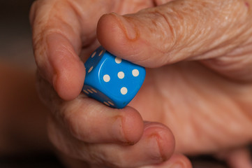Grandma rolls a blue dice.Social game. Throwing a blue cube