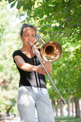 Girl learning to play trombone. Girl plays standing on the alley of a city park.