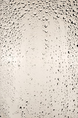Drops of water flow down the surface of the clear glass on a beige background.