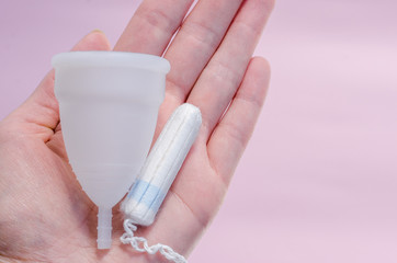 Close up of woman hand holding white menstrual cup sanitary napkin tampon on pink background health qynecology concept 