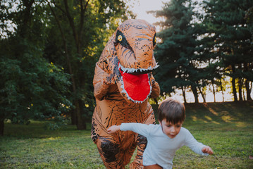 Father and son playing at the park, with a dinosaur costume, having fun with the family outdoor © oneinchpunch