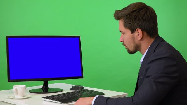 A young businessman sits in front of a computer with blue screen and shakes his head at the camera - green screen studio