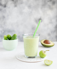 healthy smoothie with avocado cucumber apple in a glass with a straw on a light background