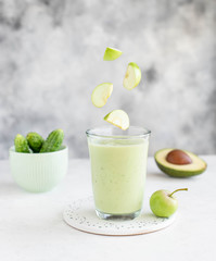 glass of smoothie with avocado cucumber and flying apple slices on a light background. healthy food concept