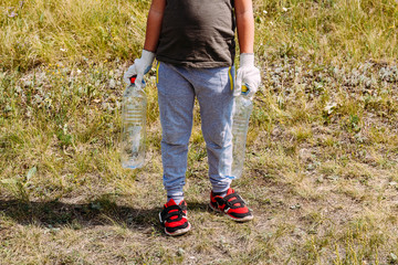 boy in working gloves removes plastic debris , holding empty plastic bottles. environmental problem