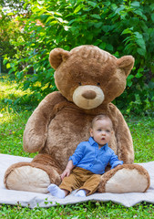 Sweet little baby boy playing with his giant teddy bear in the park
