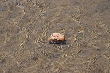 Small rock over a thin layer of moving clean water in the beach