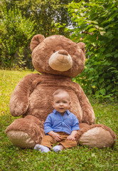 Sweet little baby boy playing with his giant teddy bear in the park