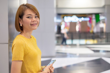 Asian young woman wear yellow shirt smile and using smartphone at plaza