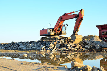 Heavy excavator working at gravel quarry unloads old concrete stones for crushing and recycling to gravel or cement. Special heavy construction equipment for road construction.