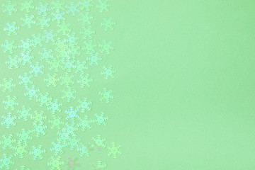 Holographic foil snowflakes confetti sparse on trendy neo mint colored background. Simple holiday...