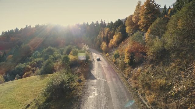 modern car drives along grey asphalt road past dense mixed forest against high hill silhouettes aerial view. Carpathian mountains, Ukraine beauty nature. Travel, summer holidays, wild recreation. 4K