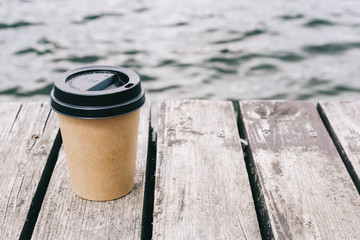 Coffee cup on sea background and brown wood. Paper cup. Mockup of coffee paper cup on brown wooden background. Copy space