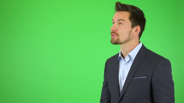 A young handsome businessman talks to the camera, something falls next to him, he gets scared, then resumes talking - green screen studio