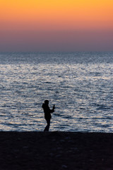 Silhouette of a person holding a smartphone on the beach in front of the sea at sunset
