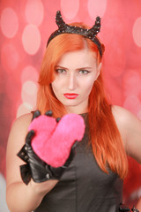 Devil girl with pink plush toy with heart shape on red background